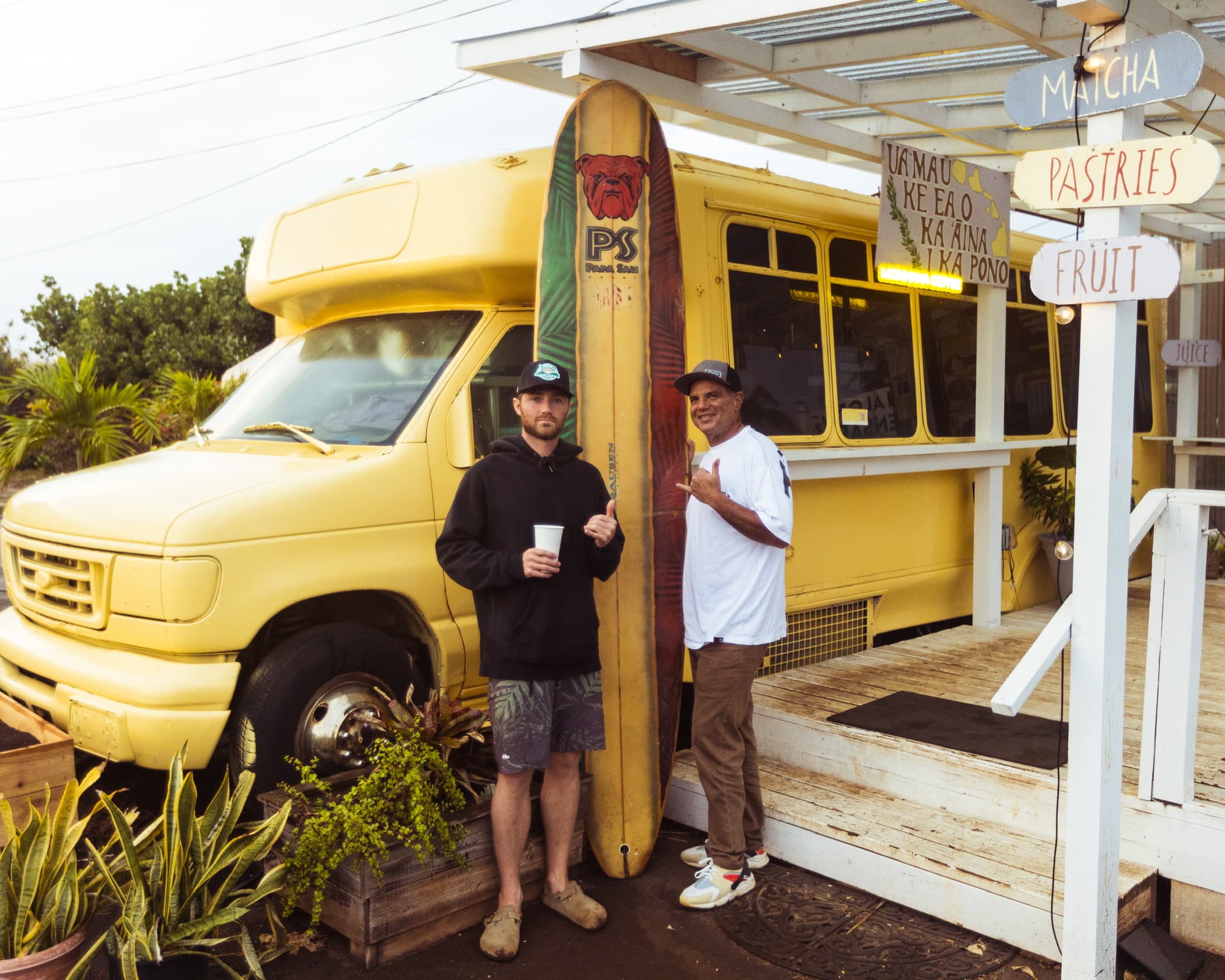 Two people standing beside the yellow Mokihana Coffee Co. bus in Kapaa